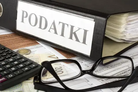 Segregator z napisem "PODATKI", okulary, kalkulator i pieniądze. Kto to jest rezydent podatkowy? To osoba, która musi rozliczyć się z dochodów.