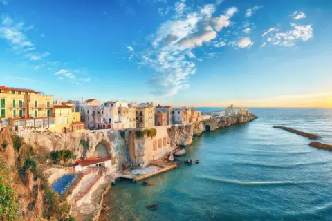 San Mennaio, un borgo sul mare con case colorate aggrappate alla scogliera, baciato dal sole al tramonto.