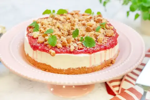 En krämig rabarber cheesecake med smulig topping och färska myntablad, serverad på ett rosa tårtfat.