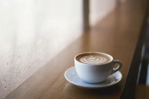 Tazza di cappuccino con latte art su un tavolino di legno, vicino a una finestra appannata. Immagina come mettere le cialde nel portafiltro per un caffè perfetto.