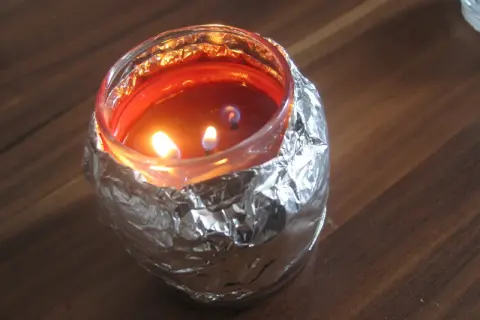 Płonąca świeca w szklanym naczyniu, owiniętym folią aluminiową, tworząc efekt tunelowania świecy.