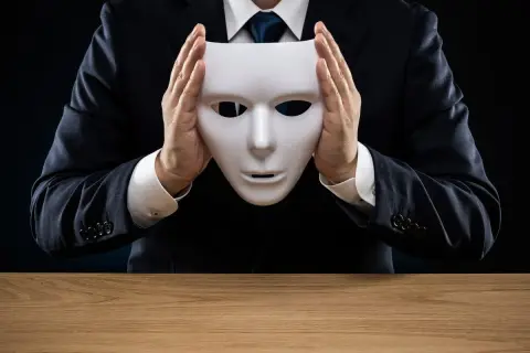Man in pak houdt wit masker voor gezicht, symboliseert psychopaat kenmerken zoals bedrog en gebrek aan empathie.