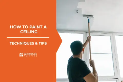 Learn how to paint a ceiling with this guide. A man uses a roller on an extension pole to apply white paint to a ceiling.