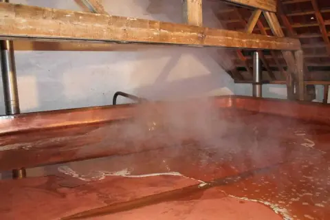 Vapore sale da una grande vasca di rame in una lambiek fabriek. La luce illumina il processo di produzione della birra.