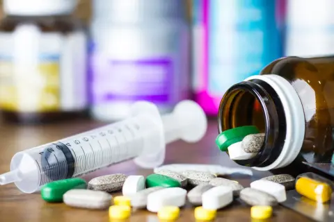 Strzykawka i tabletki, w tym zielone i żółte, rozsypane obok buteleczki. Może to być diphergan syrop w formie tabletek.