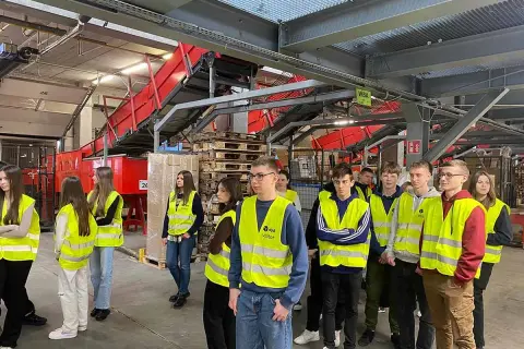 Grupa młodych ludzi w kamizelkach odblaskowych zwiedza sortownię InPost. To przyszłość pracy w logistyce.