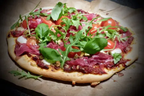 En läcker bresaola pizza med tomater, ruccola och färsk basilika.