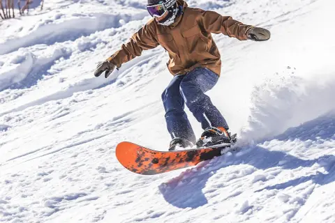 Mężczyzna na desce snowboardowej męskiej zjeżdża po ośnieżonym stoku, tworząc obłok śniegu.
