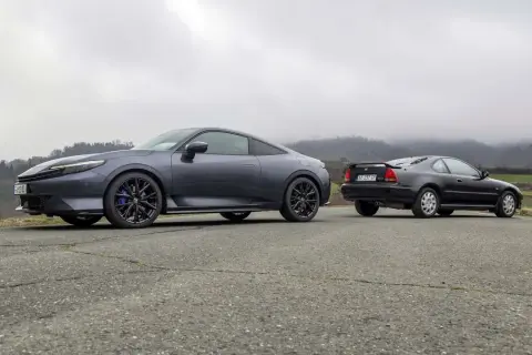 Due coupé Honda, una moderna e una classica, si incontrano su una strada di campagna. La nuova Honda Prelude 2026, grigio scuro, spicca accanto alla sua antenata.