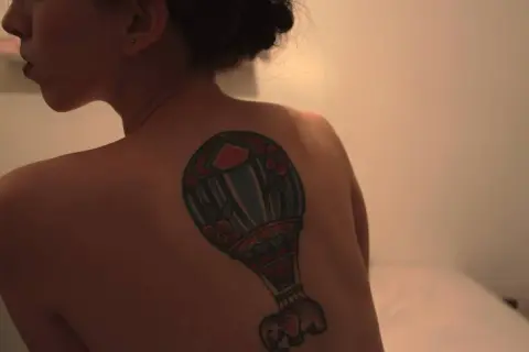 Kolorowy tatuaż balon z małym słoniem na plecach kobiety.
