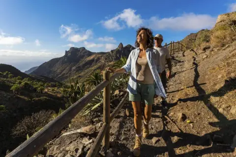 Ett par njuter av en vacker la gomera vandring i solsken, med dramatiska berg och palmer i bakgrunden.