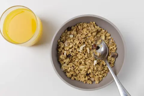 Schüssel mit dinkelflocken oder haferflocken, Nüssen und Trockenfrüchten, daneben ein Glas Orangensaft.