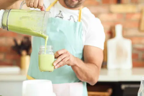 Hombre vertiendo un batido verde cremoso, ideal para quienes buscan alternativas a los tipos de leches vegetales.