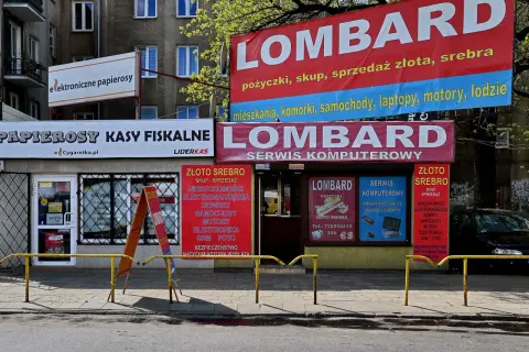 Szyldy lombardu i sklepów z elektroniką i papierosami na tle budynku mieszkalnego.