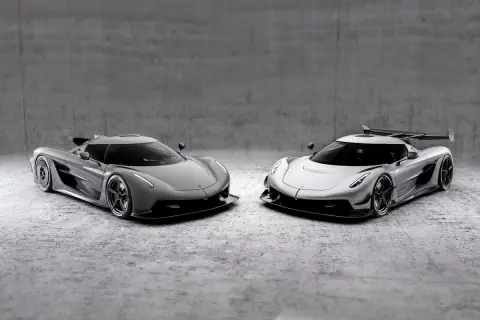 Dwa lśniące Koenigsegg Jesko, jeden szary, drugi srebrny, stoją obok siebie na betonowym tle.