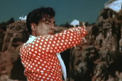Un hombre con camisa de lunares rojos y blancos, bailando con pasión. Su gesto evoca la fuerza de la contrahecha.