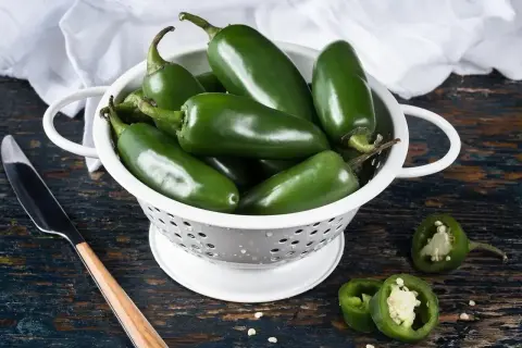 Świeże, zielone papryczki **jalapeno** w durszlaku, gotowe do przygotowania pikantnych potraw. Kilka przekrojonych sztuk pokazuje ich wnętrze.
