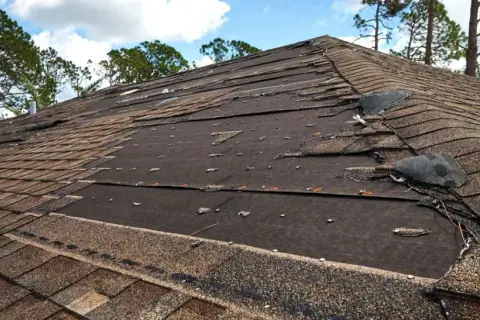 Damaged asphalt shingle roof repair needed. Many shingles are torn, lifted, or missing, exposing the underlayment.