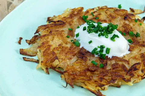 Une galette de pomme de terre dorée et croustillante, garnie d'une cuillère de crème fraîche et de ciboule ciselée. Un délice simple et savoureux.