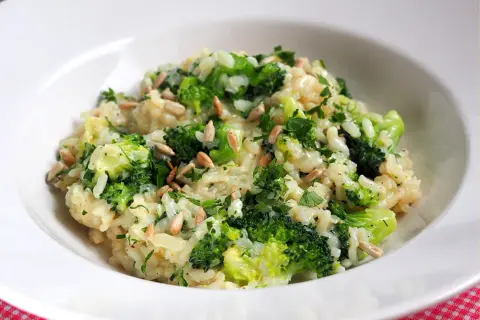 Kremowe risotto z brokułami, posypane słonecznikiem i natką pietruszki, podane w białej misce.