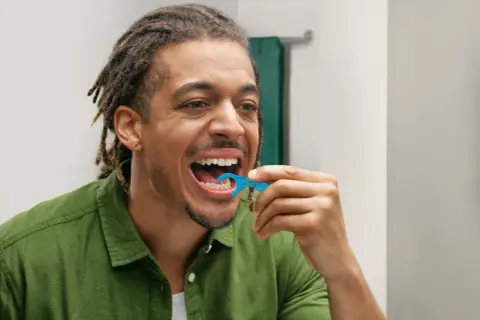 Uomo con dreadlocks usa una forcella tendifilo interdentale blu per pulire i denti.