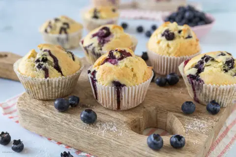 Frisch gebackene Blaubeermuffins, die nach den besten Muffin Rezepten aussehen, liegen auf einem Holzbrett.