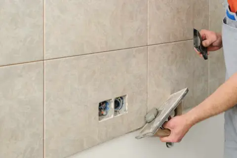 Un carreleur applique un joint époxy sur des carreaux muraux. Il utilise une taloche pour étaler le mortier.