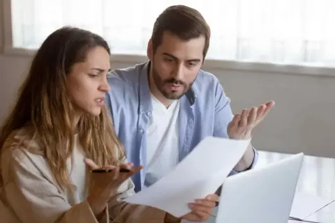 Un couple discute, perplexe, devant des documents. La question "faut il payer les droits de succession avant d'hériter ?" les préoccupe.