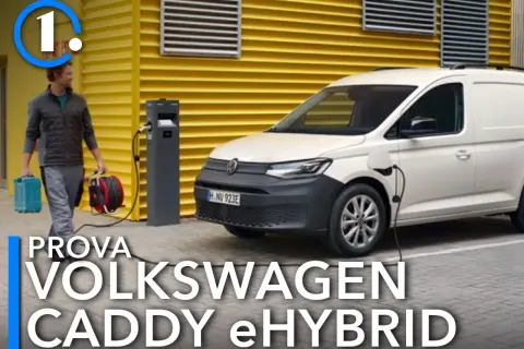 Un uomo porta cavi per caricare il Volkswagen Caddy eHybrid, un furgone bianco parcheggiato vicino a una stazione di ricarica.