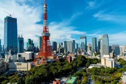 Tokio Tower góruje nad nowoczesnym miastem z wieżowcami w budowie i zielonymi drzewami.
