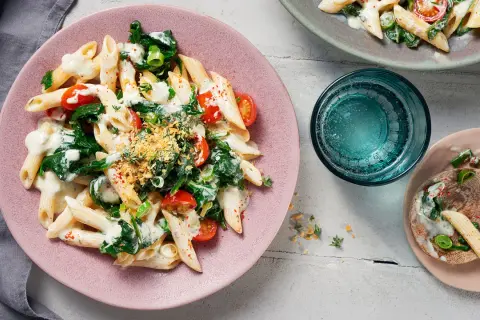 Penne mit Spinat und cremiger Sauce auf einem rosa Teller, garniert mit Kirschtomaten und Kräutern.