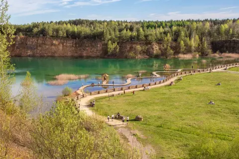 Malowniczy park Gródek w Jaworznie z turkusową wodą, drewnianymi kładkami i zielonymi terenami rekreacyjnymi.