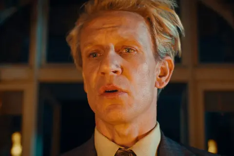 En man med blont hår och en grå kostym, med en blick som säger "och så var de bara en".