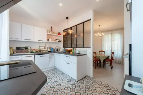 Carrelage décoratif au sol pour la délimitation carrelage cuisine salon. Une cuisine moderne blanche ouverte sur une salle à manger avec lustre.