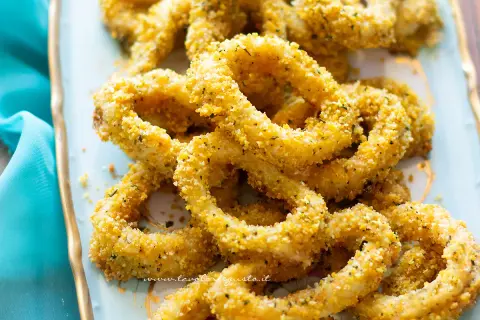Anelli di totano al forno, dorati e croccanti, serviti su un piatto azzurro con un tovagliolo turchese.