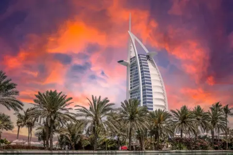 Zachód słońca nad Dubajem z palmami i hotelem Burdż al-Arab. Zastanawiasz się, ile kosztuje wycieczka do Dubaju?