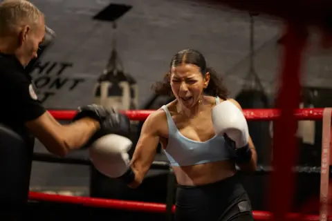 Intense boxing warm up: a woman throws a punch with fierce determination as her trainer holds pads.