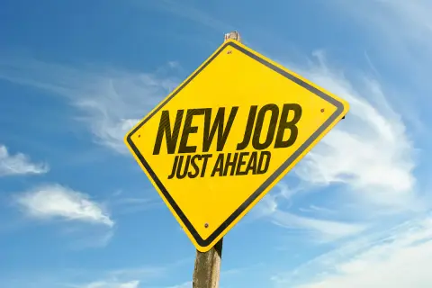 Gul varningsskylt med texten "NEW JOB JUST AHEAD" mot en blå himmel med moln. Perfekt för den som trivs inte på jobbet och söker nya utmaningar.