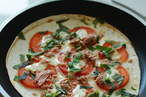 Pyszna pizza z tortilli z tuńczykiem, pomidorami i bazylią, przygotowywana na patelni.