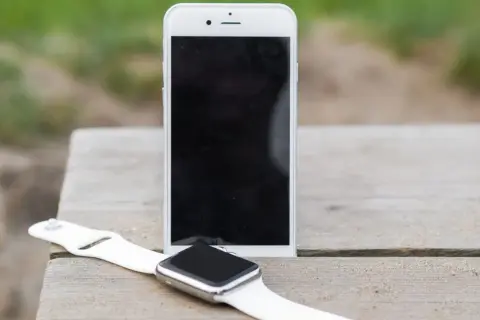 Biały smartwatch i smartfon leżą na drewnianym stole. Dowiedz się, jak sparować zegarek z telefonem, by cieszyć się nowymi możliwościami.