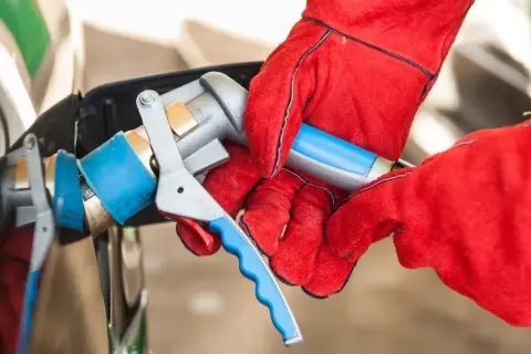 Ręce w czerwonych rękawicach podłączają pistolet do tankowania LPG. Sprawdzanie aktualnej lpg cena to klucz do oszczędności.