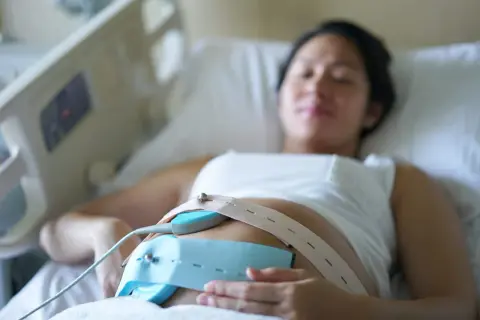 Une femme enceinte est allongée, un moniteur de rythme cardiaque fœtal est fixé sur son ventre. Ce monitoring sert à surveiller le bien-être du bébé.