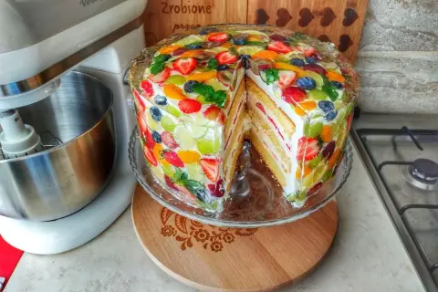 Kolorowy tort z galaretką i owocami, gdzie dekoracyjne układanie owoców tworzy tęczową mozaikę.