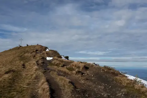 Pfad führt zu einem Gipfelkreuz auf einem **hohen Freschen**. Wanderer genießen die Aussicht auf die Alpen.
