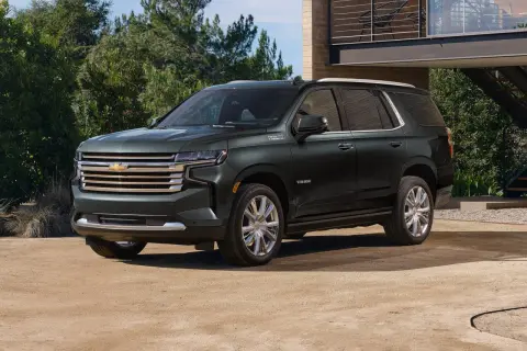 Ciemnozielony Chevrolet Tahoe High Country z chromowanymi felgami stoi przed nowoczesnym domem.