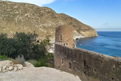 Ruinas de un castillo en cala san pedro, con el mar azul y montañas al fondo.