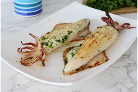 Due calamari alla griglia, conditi con erbe aromatiche, serviti su un piatto bianco.