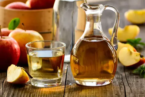 Aceto di mele in caraffa e bicchiere, con mele fresche. Un rimedio naturale per un bucato morbido.