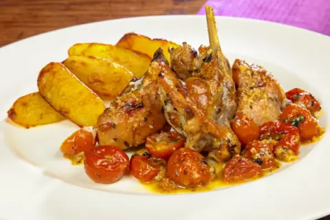 Piatto di coniglio al forno con patate arrosto e pomodorini confit.