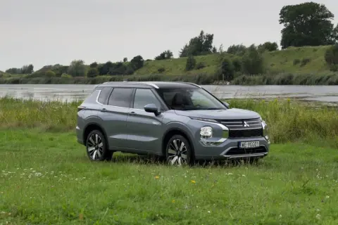 Szary Mitsubishi Outlander PHEV zaparkowany na łące nad jeziorem.